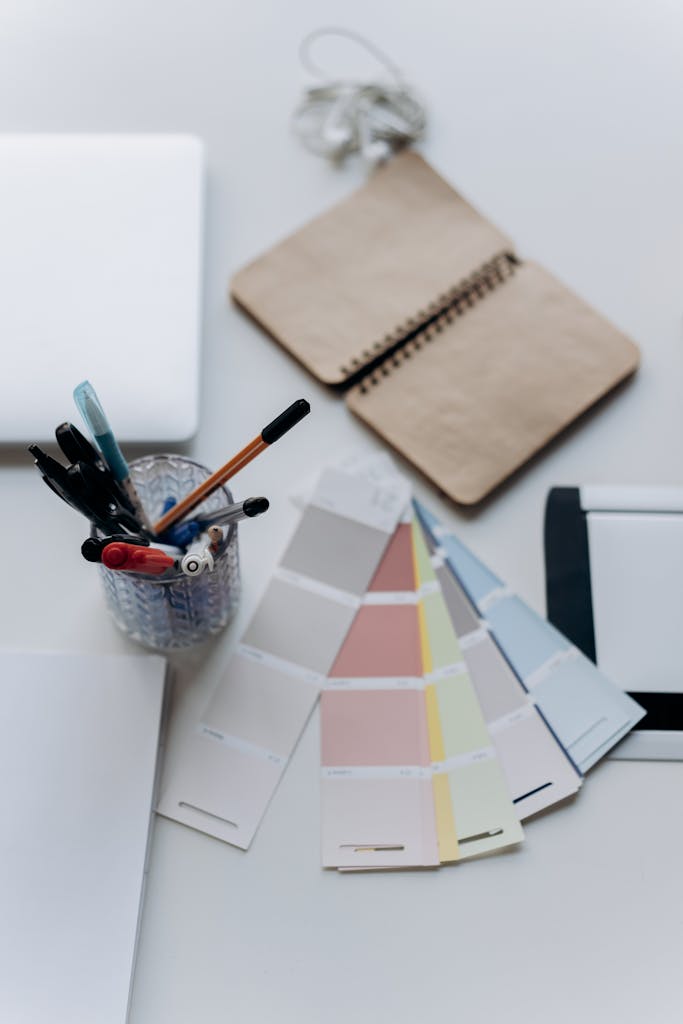 Organized workspace featuring color swatches, notebook, laptop, and stationery for design projects.