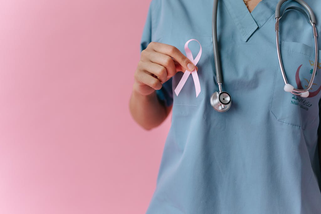 Healthcare worker in scrubs holds a pink breast cancer awareness ribbon symbolizing support.